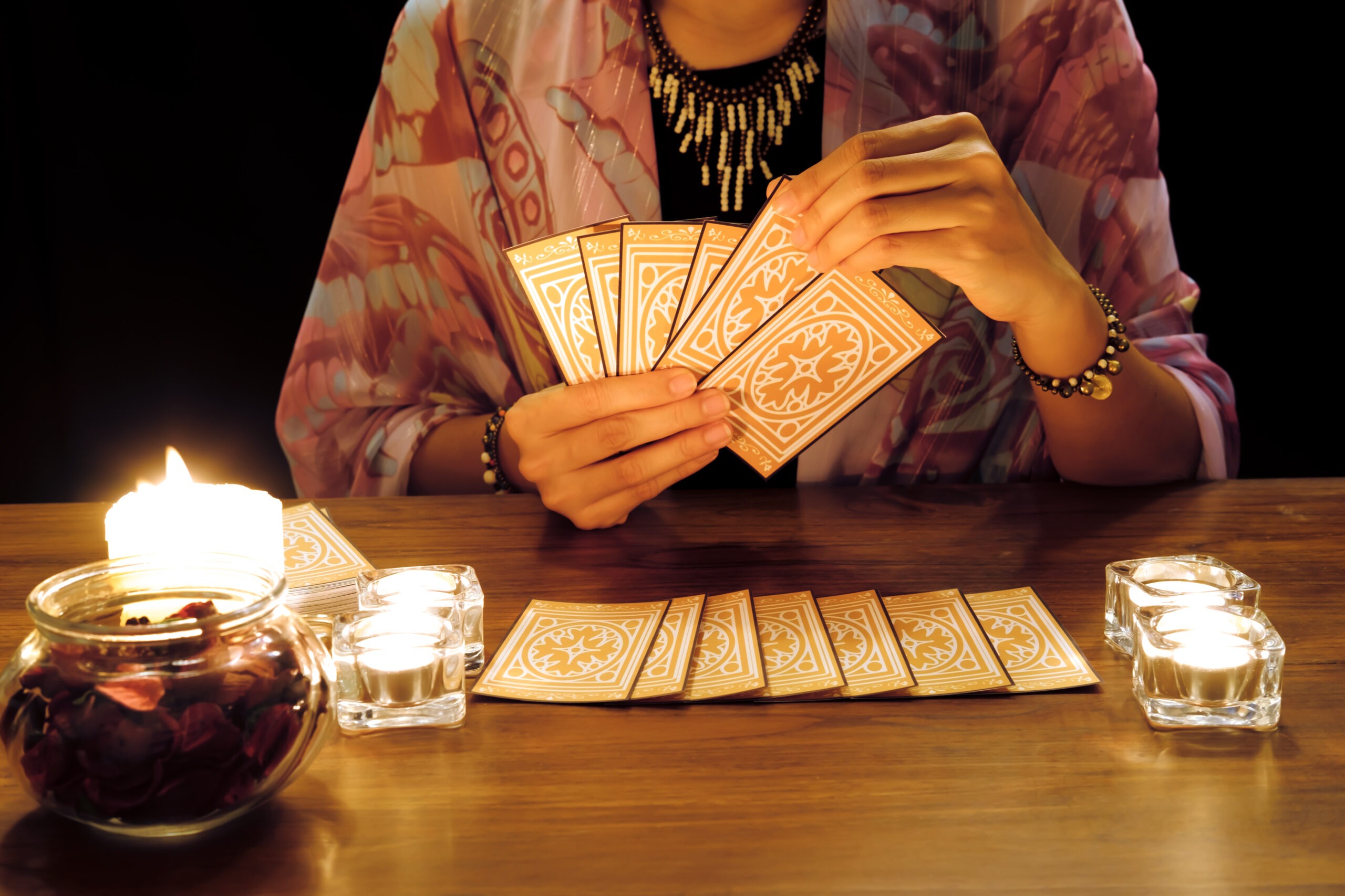 A person in a colorful shawl holds tarot cards over a wooden table