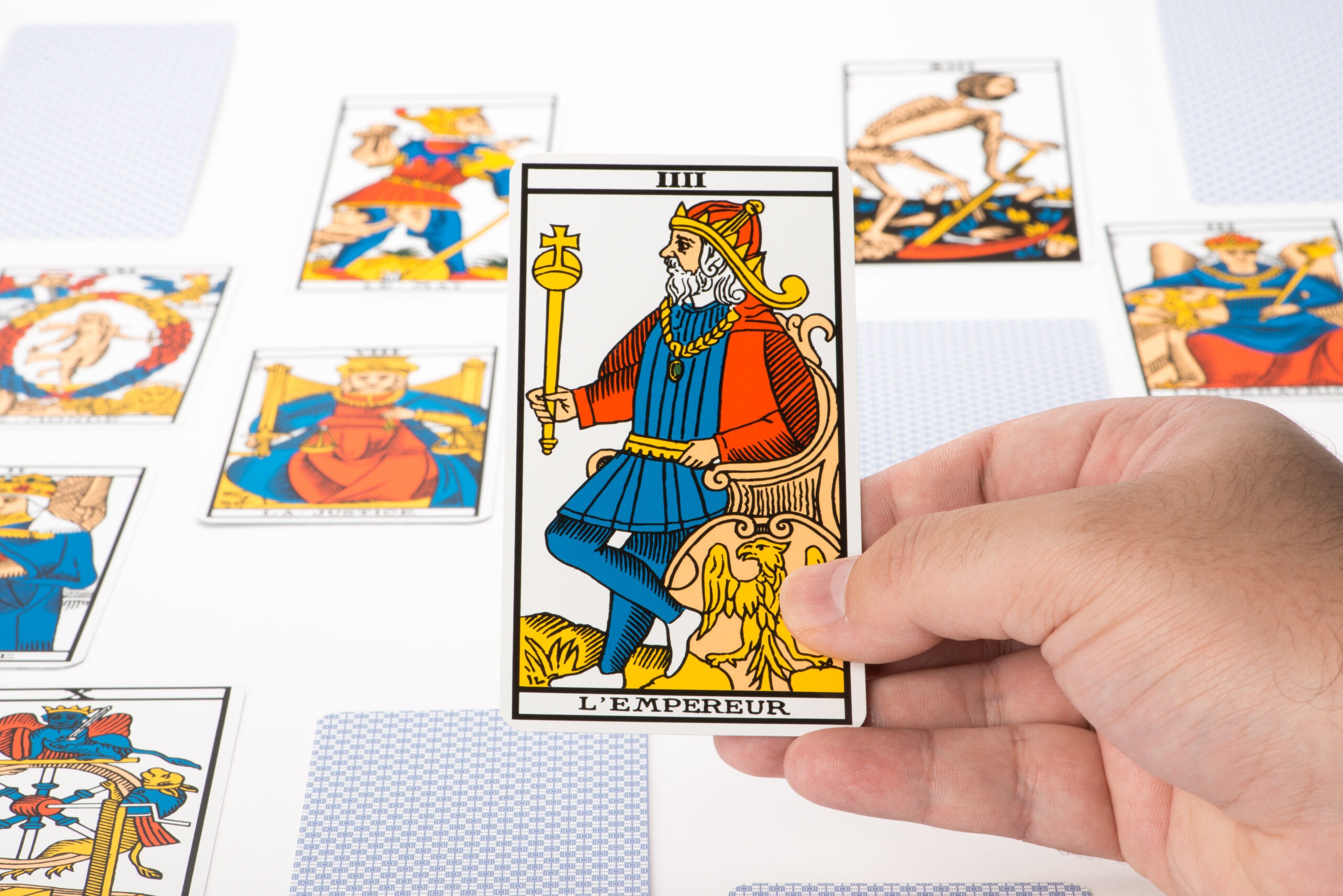A hand holds the "L'Empereur" tarot card